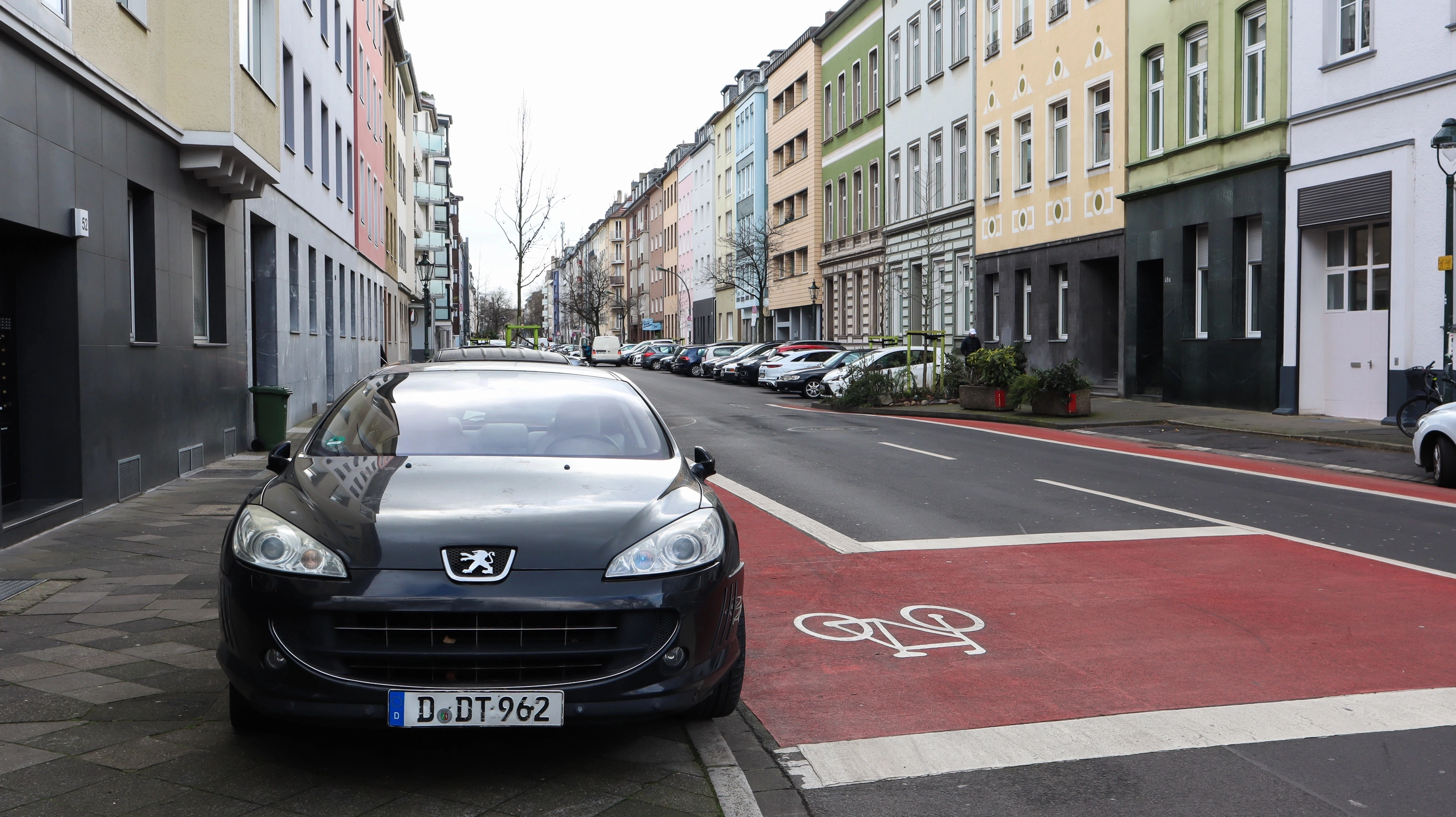 Een geparkeerde auto bij een rode fietsstrook in een kleurrijke woonstraat in Düsseldorf; in de milieuzone heb je een milieusticker nodig